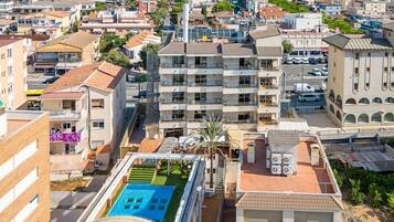 Un edificio de gran altura con varios balcones, una piscina en la azotea y vistas del entorno urbano.