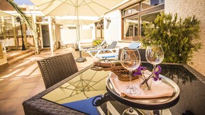 An outdoor patio with a glass table, wicker chairs, and umbrellas. - HOTEL VICTORIA (Calafell)