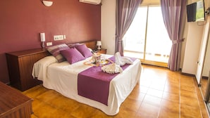 A hotel room with a bed, a bedside table, a TV, and a window with curtains. - HOTEL VICTORIA (Calafell)