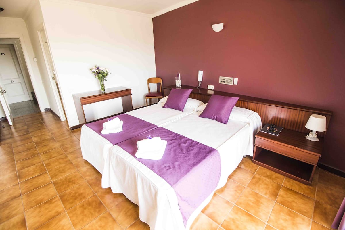 A hotel room with a large bed, two bedside tables, a nightstand, a chair, and a small desk with a vase of flowers.