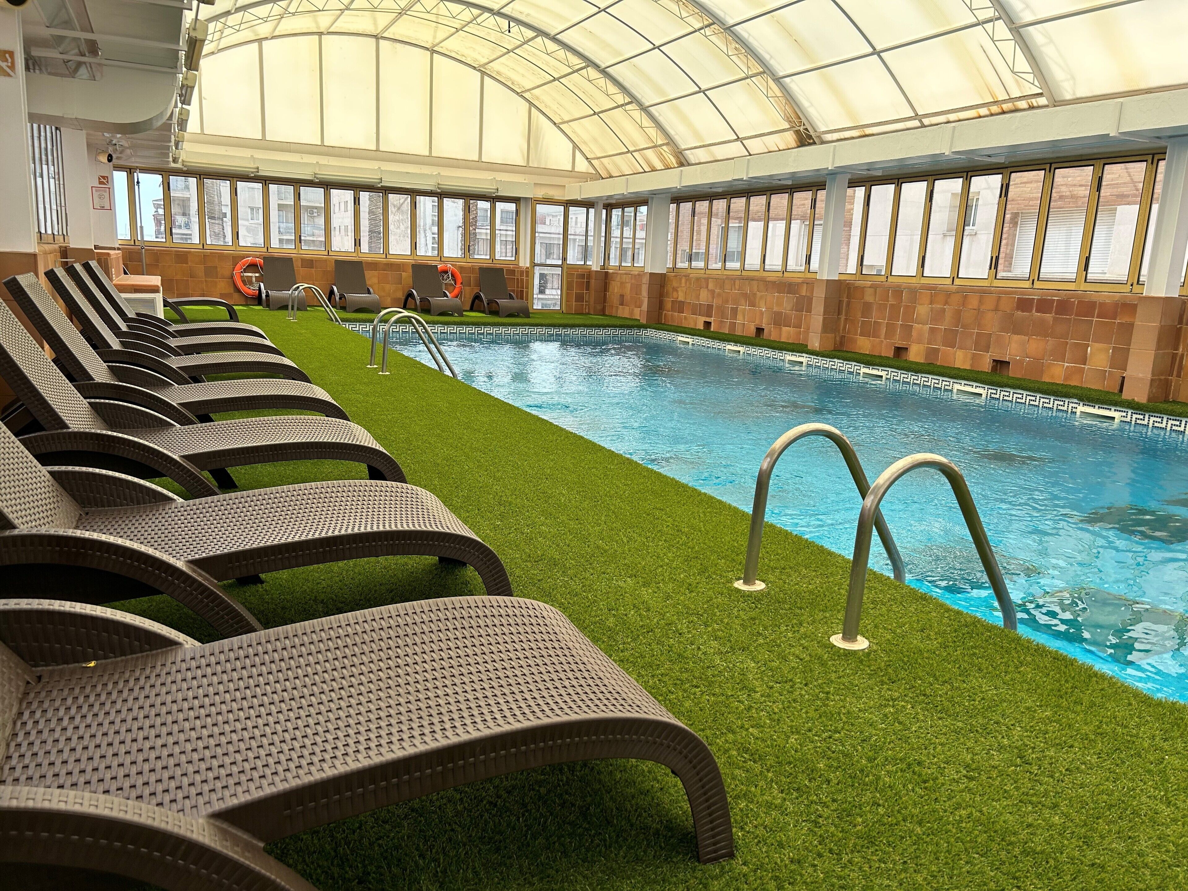 A pool area with lounge chairs and a glass ceiling.