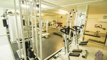 Un gimnasio con diversas máquinas de ejercicio, espejos y suelo de baldosas.
