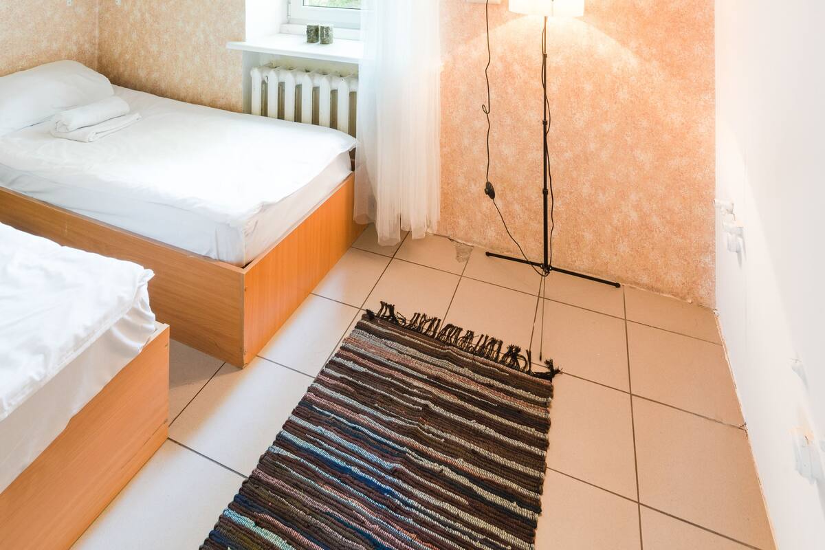 Un dormitorio con una cama, una ventana con cortinas, un radiador, una lámpara de pared y una lámpara colgante.