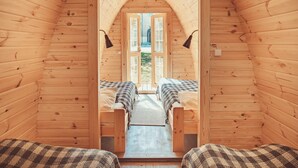 A wooden cabin with two beds, a central archway, and a view of the outdoors. - Downtown Forest Hostel & Camping (Vilnius)