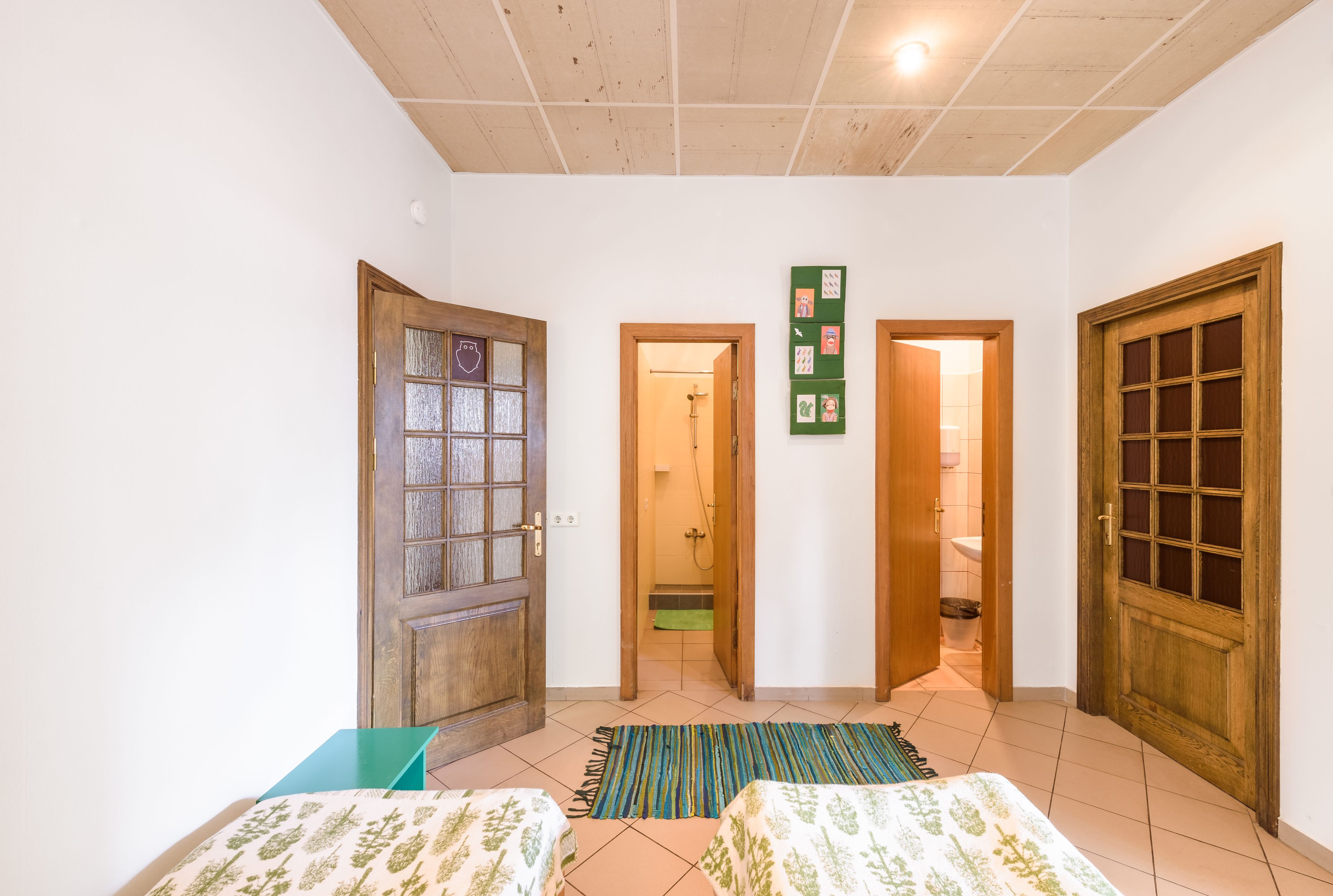 A room with two beds, a wooden door, a green mat, and a small table.