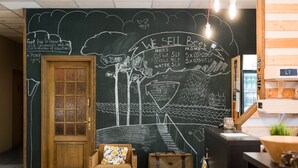 A room with a wooden door, a wicker chair, a suitcase, and a chalkboard wall with text and drawings. - Downtown Forest Hostel & Camping (Vilnius)