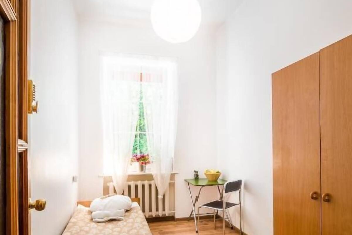 Un dormitorio con una cama, un armario de madera, una mesita con una silla y una ventana con cortina.
