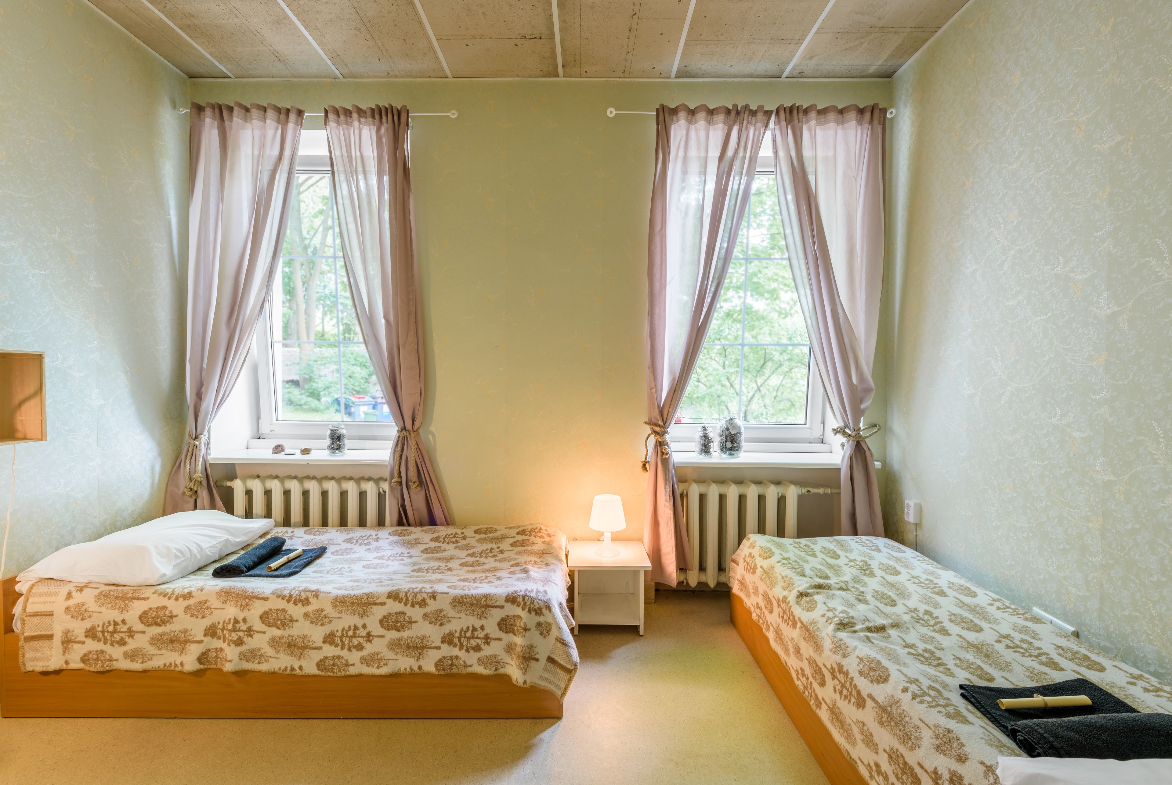 Una habitación con dos camas, una mesita de noche con lámpara y una ventana con cortinas.