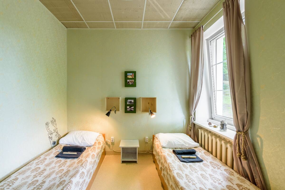 Una habitación con dos camas, una mesita y un ventanal con cortinas.