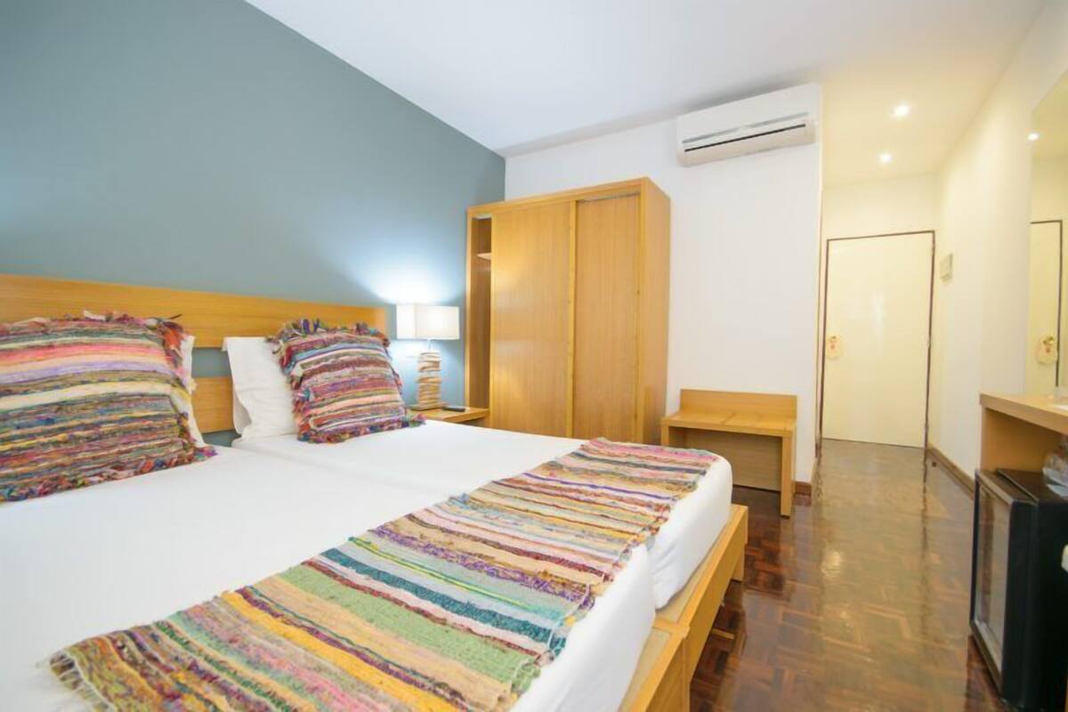Une chambre d’hôtel avec un grand lit, une armoire en bois, un banc et un bureau avec un miroir.