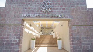 De ingang van Hotel Porto Grande, met een gevel van baksteen, een centrale trap en potplanten aan weerszijden.