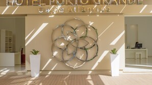 Een moderne hotel lobby met een groot abstract kunstwerk aan de wand, twee potplanten en een receptiebalie met een computer.