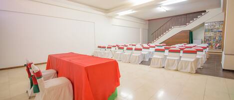 A conference room with a red table, white chairs with green sashes, and a staircase in the background.