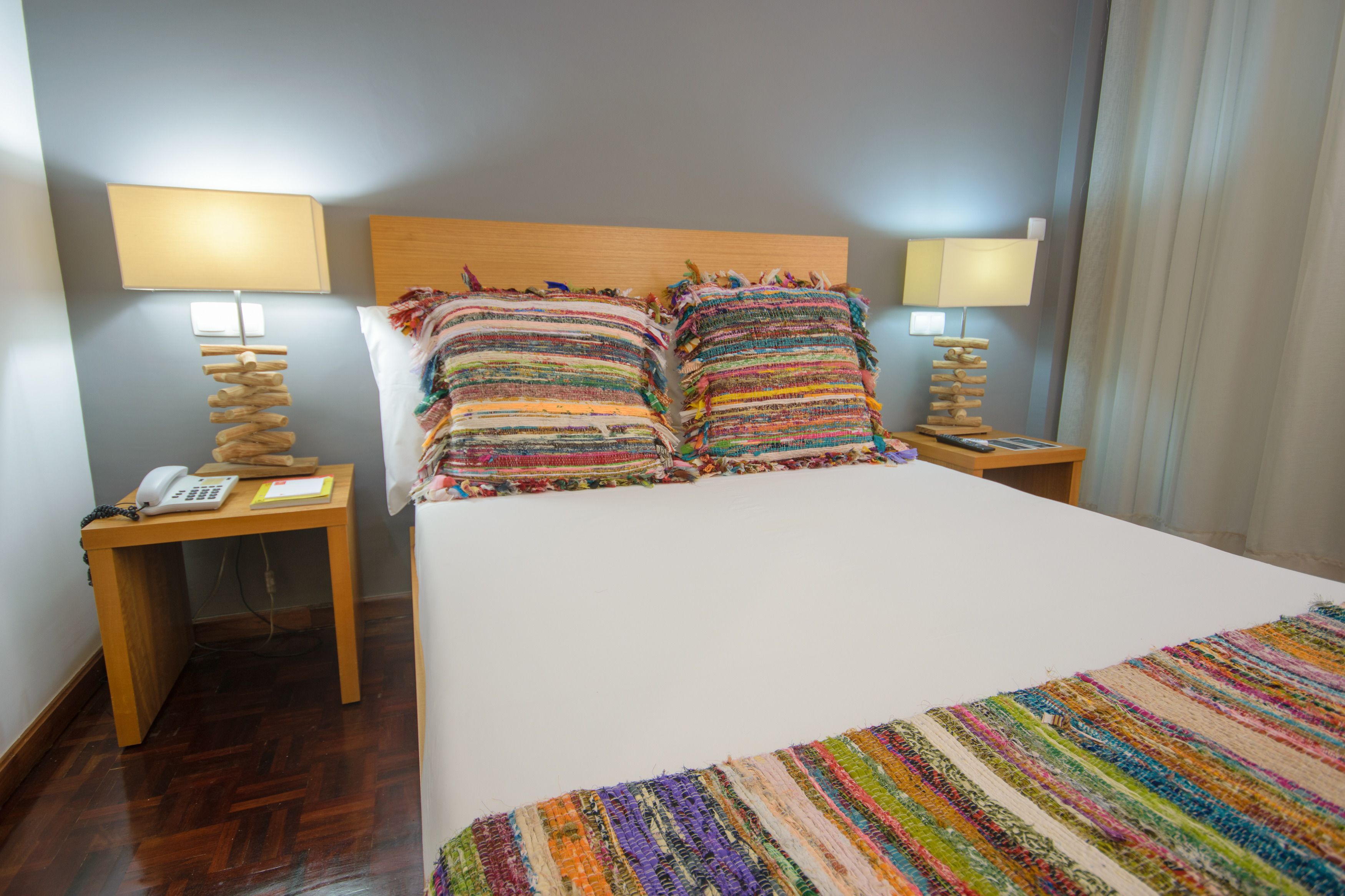A hotel room with a wooden headboard, two bedside tables with lamps, a telephone, and a colorful striped blanket.
