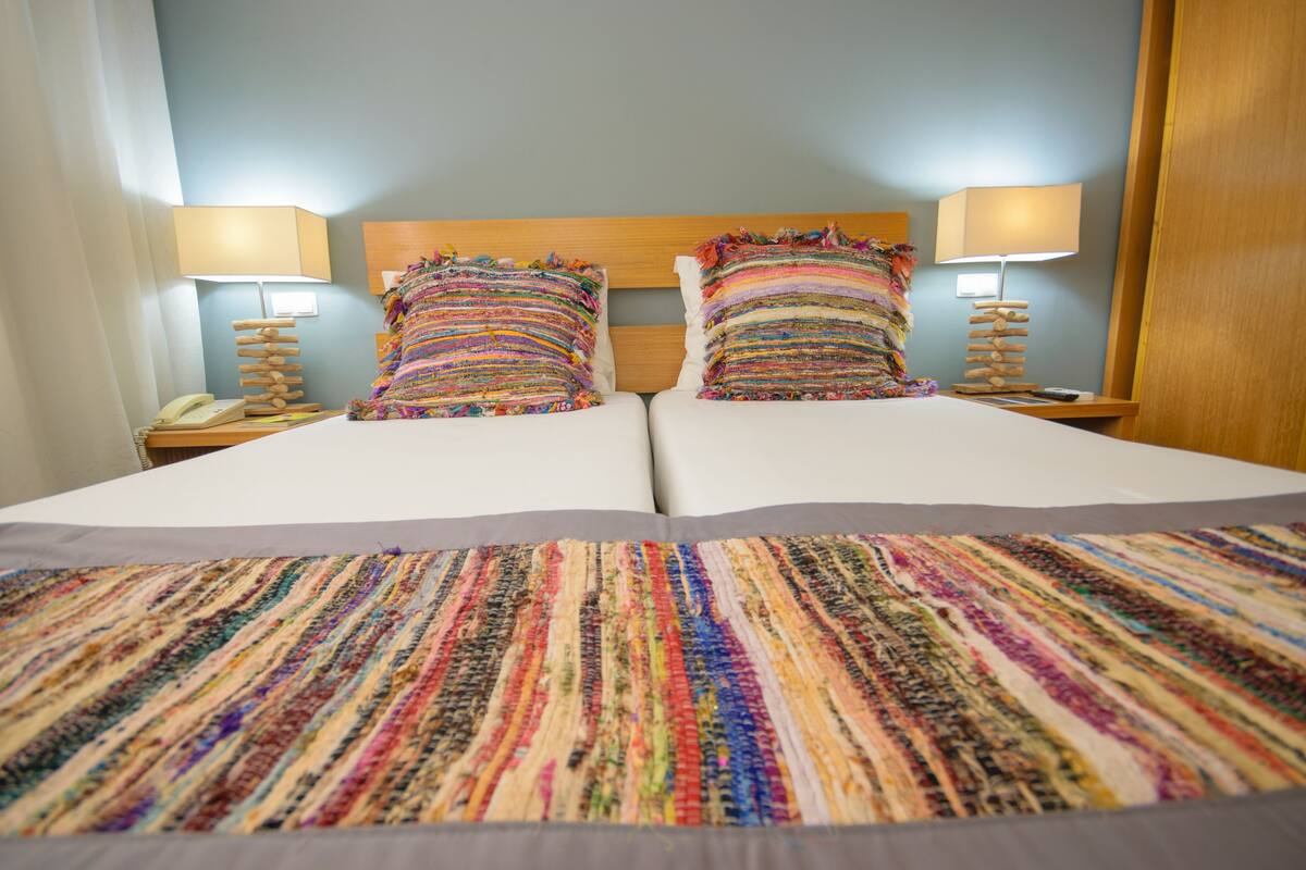 Un lit double avec une couvre-lit rayée aux couleurs vives, deux lampes de chevet et une tête de lit en bois.