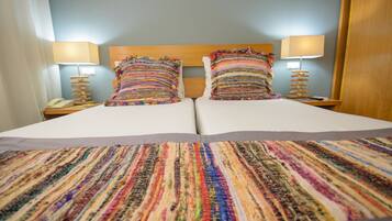 A double bed with a colorful striped bedspread, two bedside lamps, and a wooden headboard.