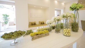 Een receptie met een witte balie, vazen met bloemen en een zithoek met kussens.