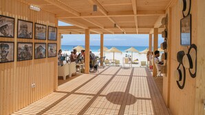 Een houten terras met tafels en stoelen, met uitzicht op het strand.
