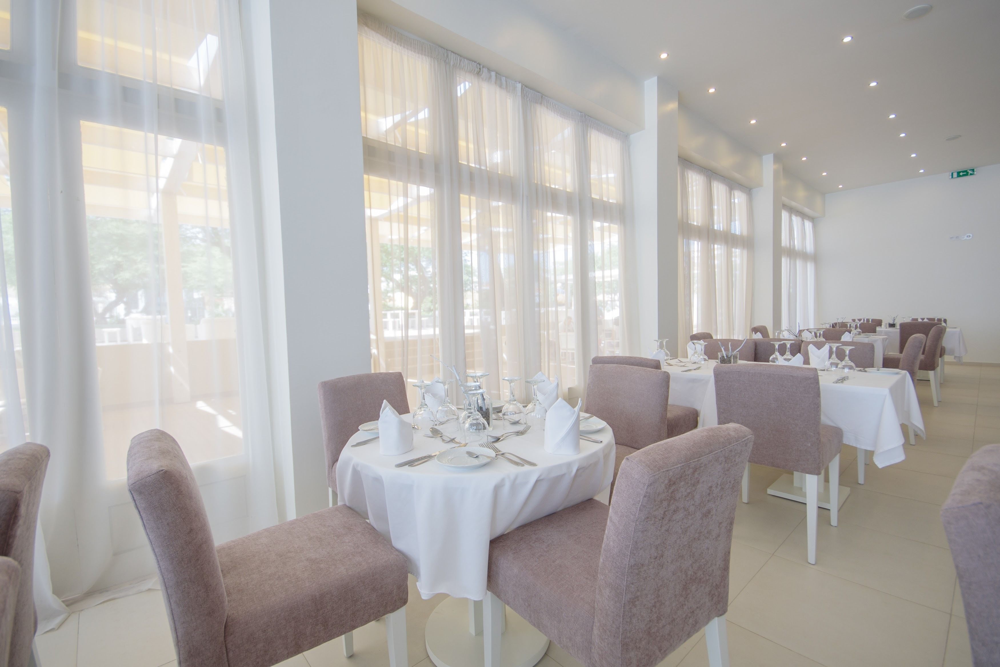 A dining area with round tables set for four, each with white tablecloths and silverware.