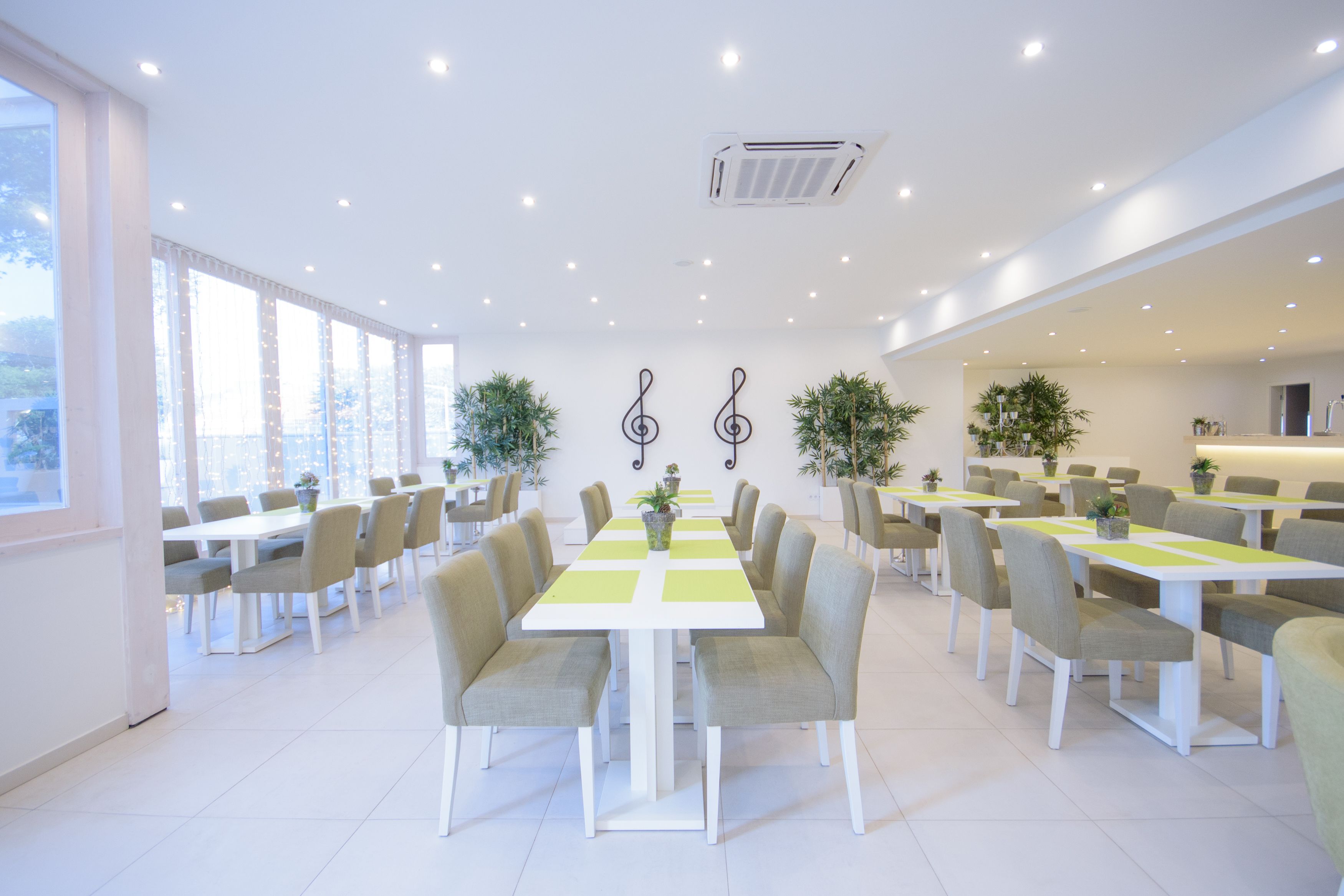 Un comedor amplio con varias mesas y sillas, ventanas grandes y plantas en macetas.