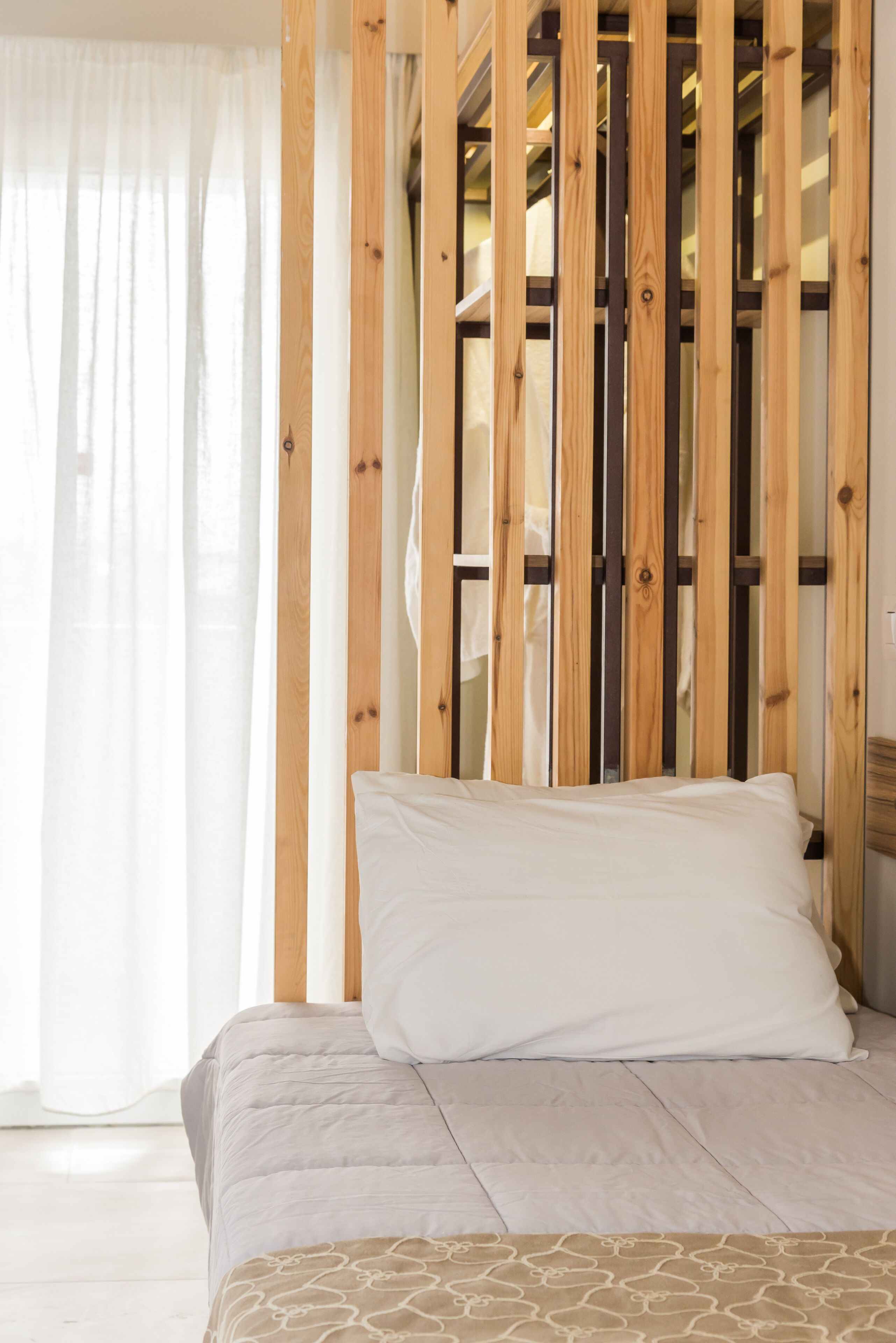 Ein Bett mit beiger Bettdecke, einem weißen Kissen und einem Holzkopfbrett mit vertikalen Lamellen.