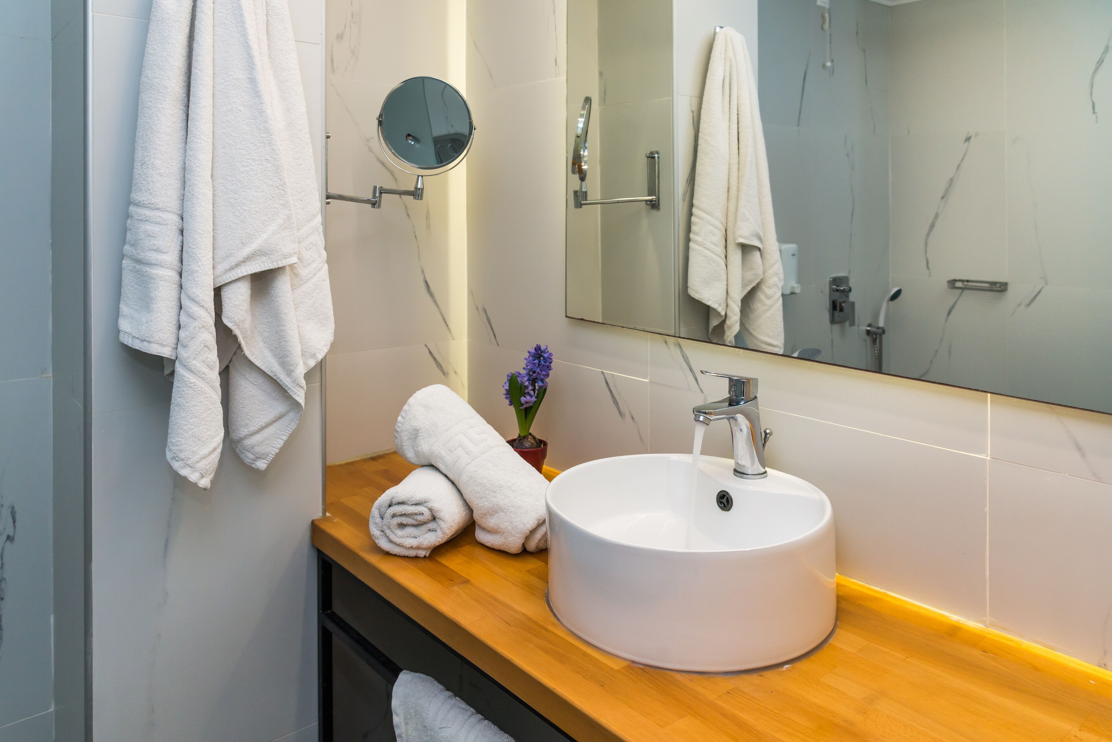 A bathroom with a wooden vanity, a white sink, a round mirror, and two towels hanging on the wall.