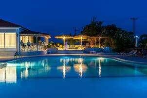 Una piscina con lettini e ombrelloni, una zona relax coperta e un edificio con tetto in tegole.
