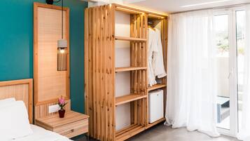 A modern hotel room with a wooden wardrobe, a small table with a potted plant, a bed with white linens, and a sliding glass door to the outside.