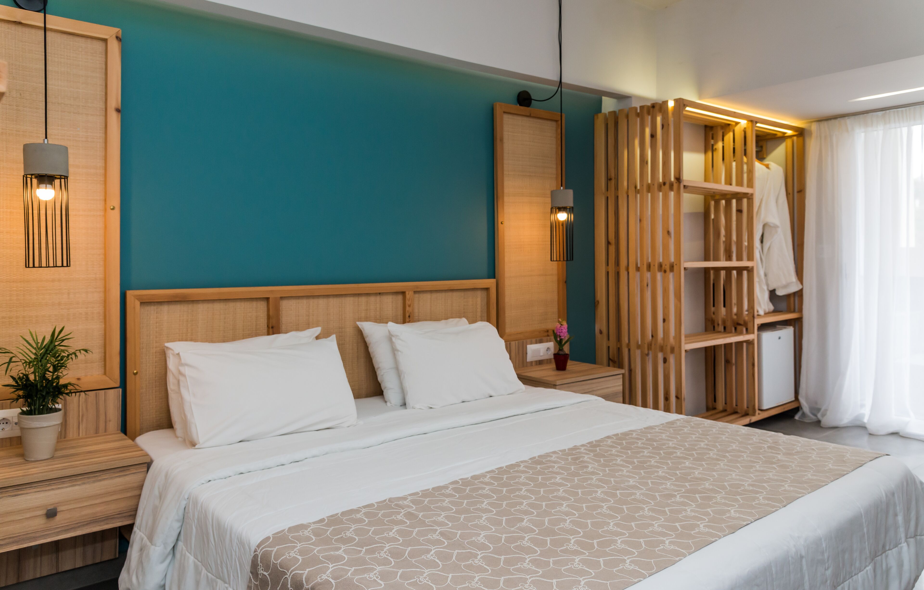 A modern hotel room with a large bed, wooden headboard, and a teal accent wall.