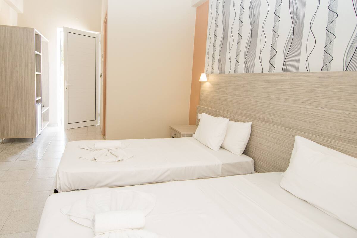 A hotel room with two beds, a wardrobe, and a nightstand.