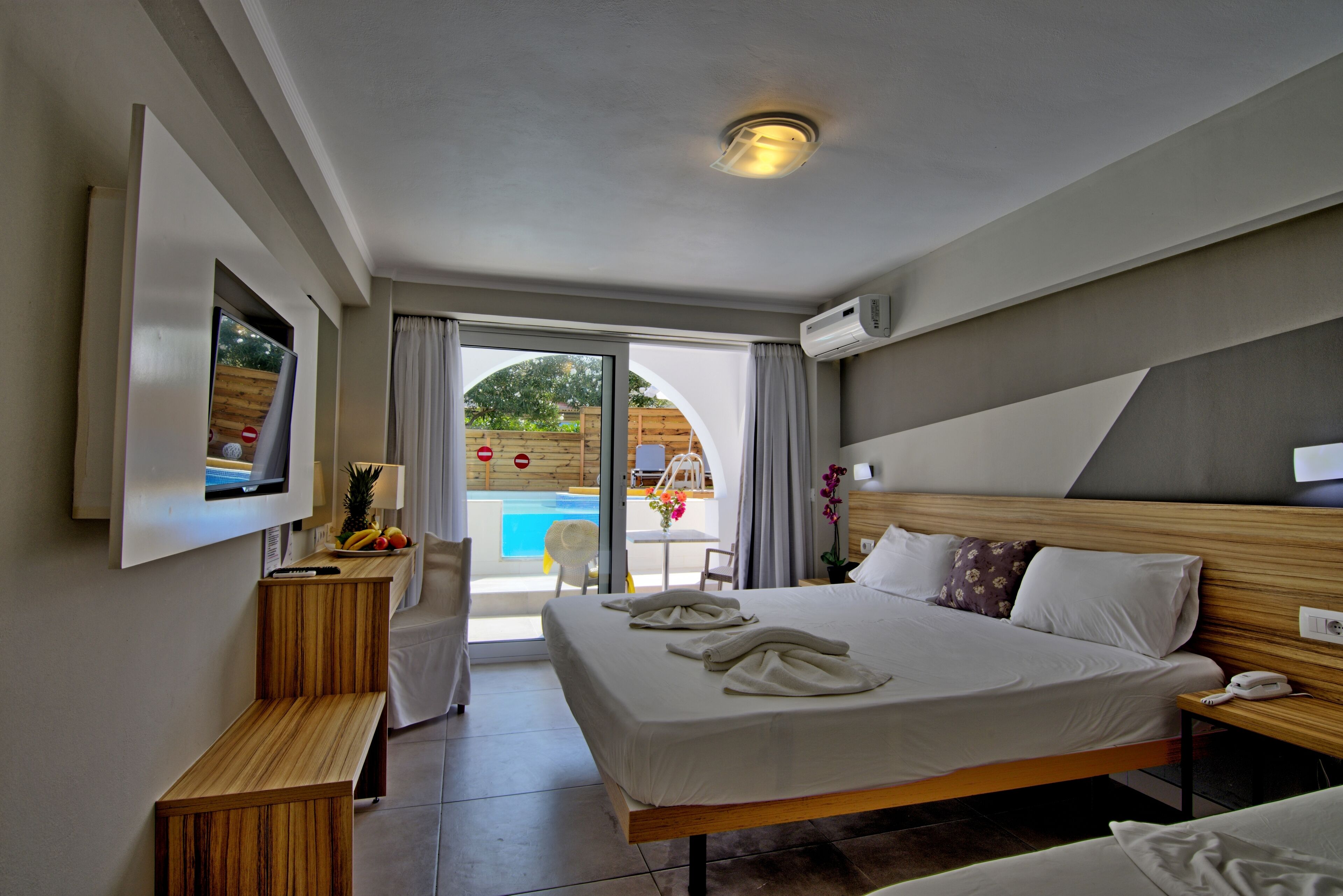 Ein Hotelzimmer mit Bett, Fernseher, Schreibtisch und Blick auf einen Außenpool.