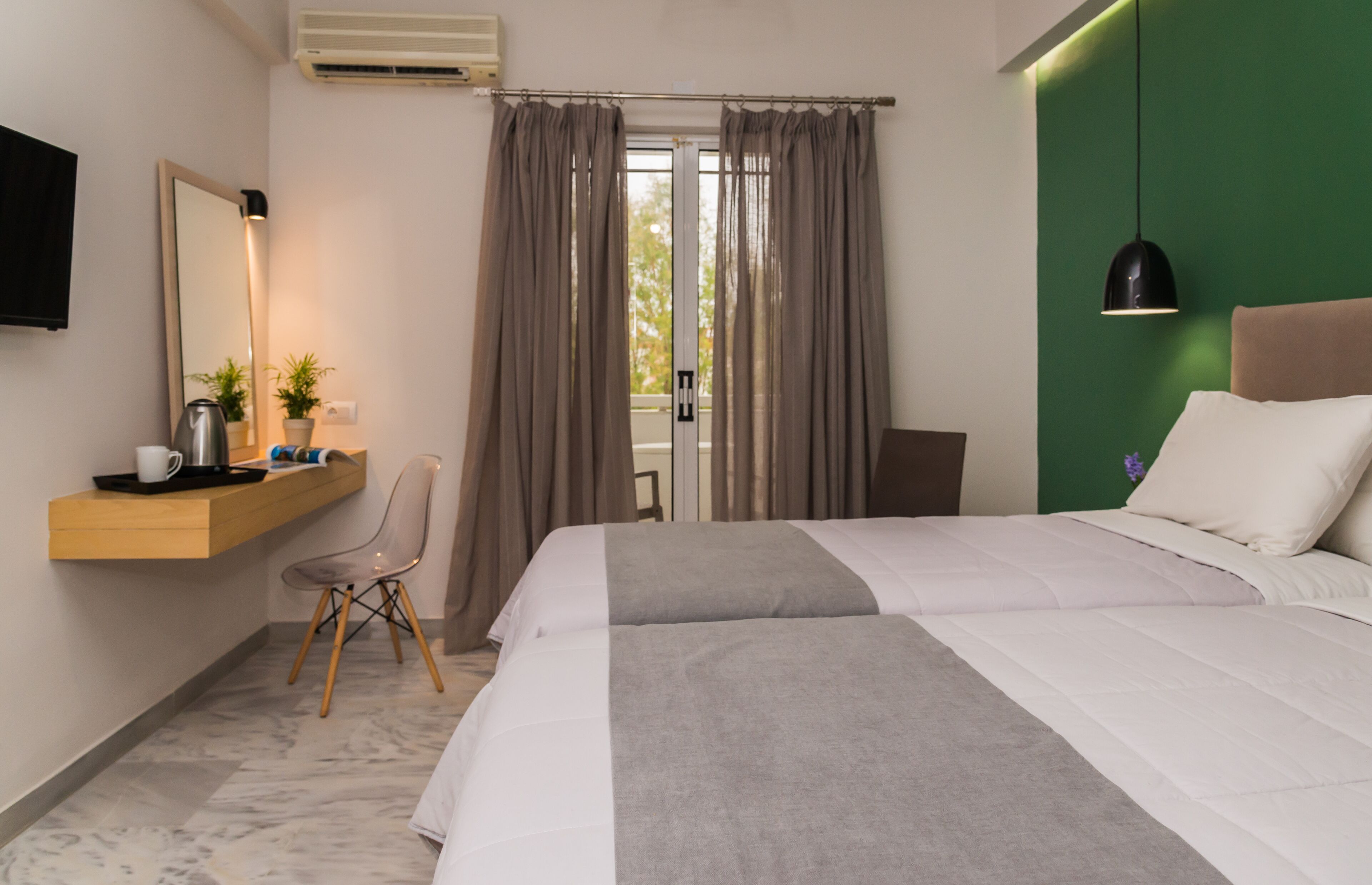 Una habitación de hotel moderna con una cama grande, un escritorio con una silla, un espejo y una pared de acento verde.