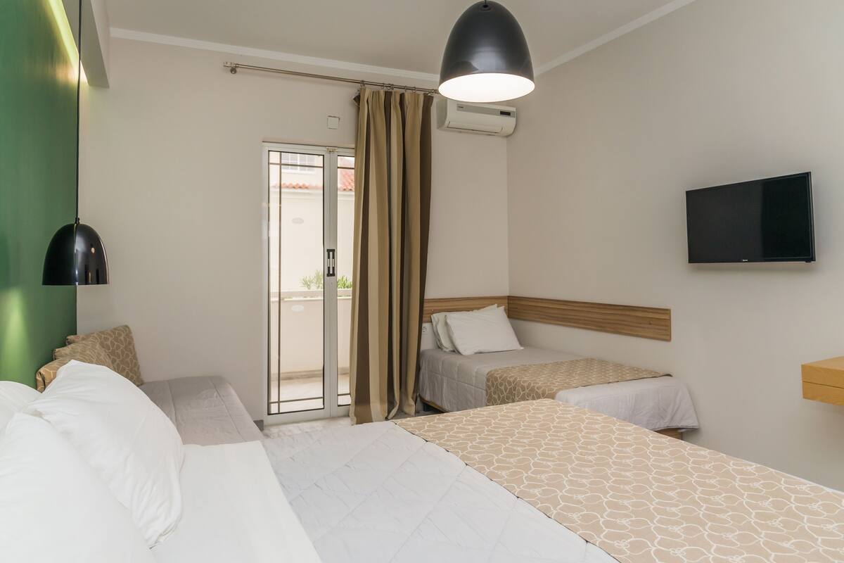 A hotel room with two beds, a television, and a sliding glass door to the outside.