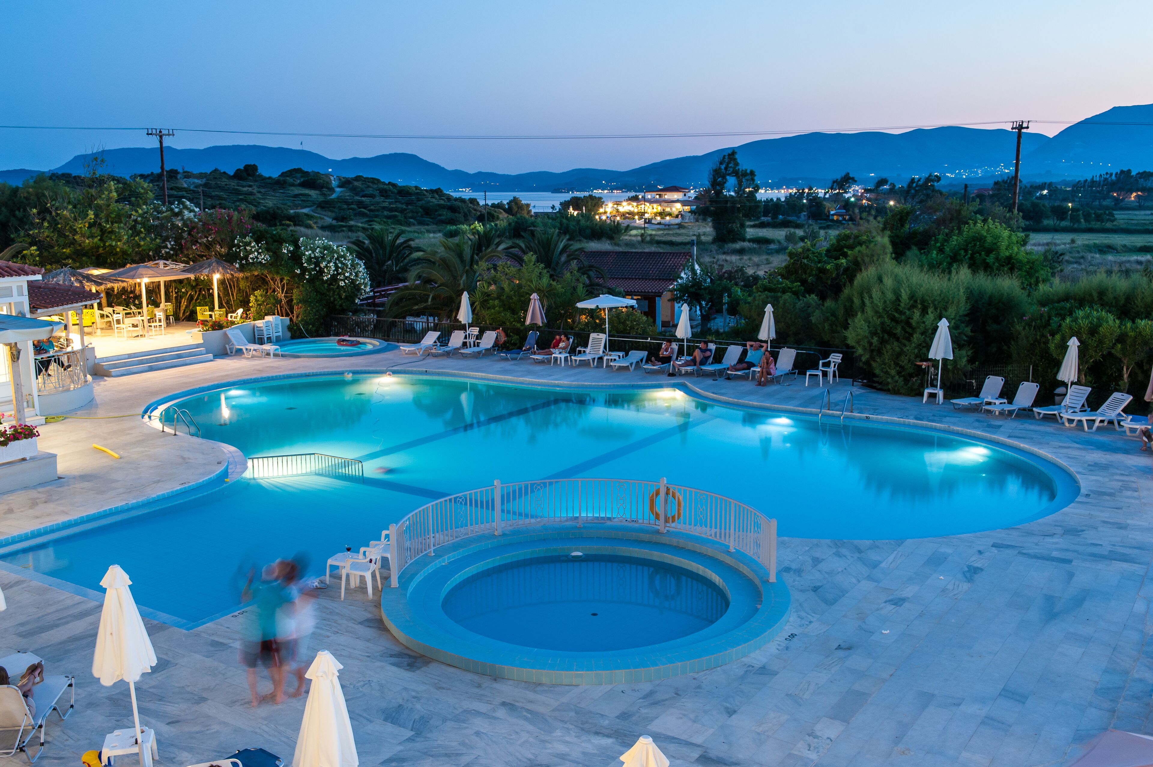 Piscina con varias secciones y un solárium con sillones de playa y sombrillas.