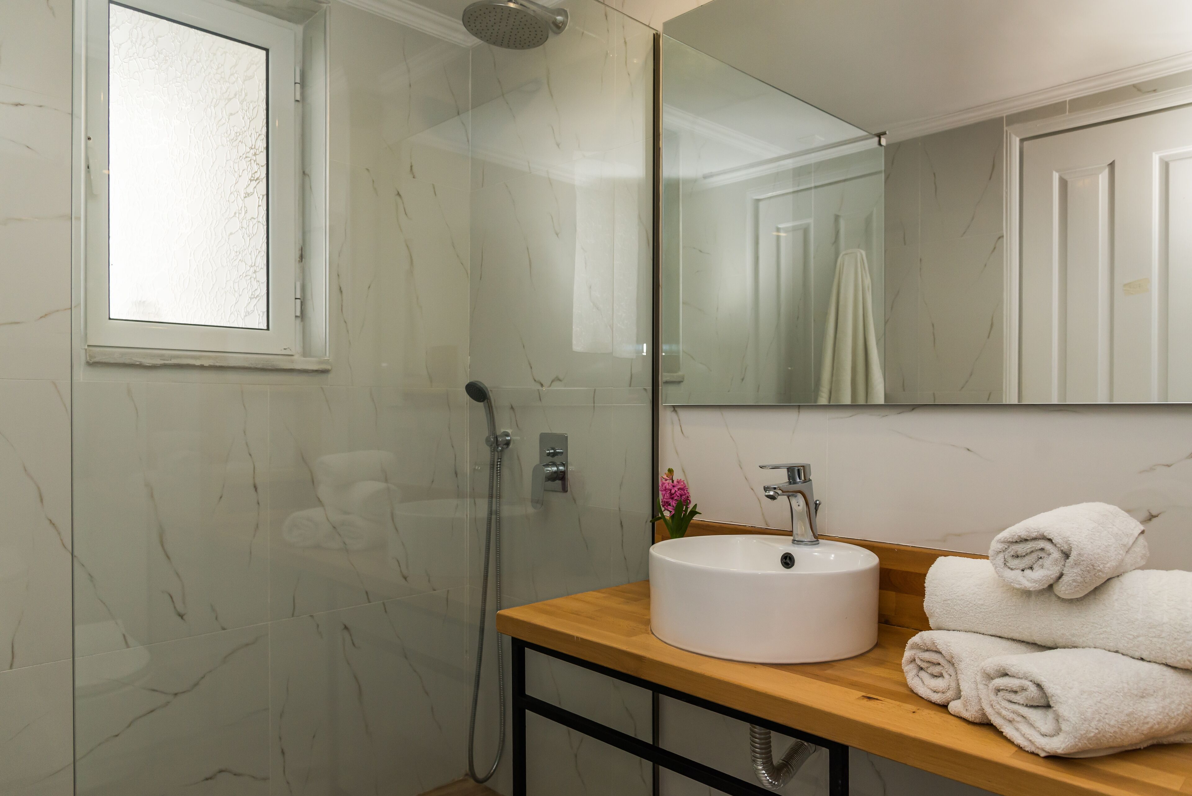 A bathroom with a glass-enclosed shower, a wooden vanity with a white sink, and a mirror above the sink.