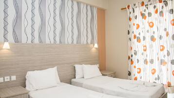 A hotel room with two single beds, a wooden headboard, a patterned wall, and a curtain with a geometric design.