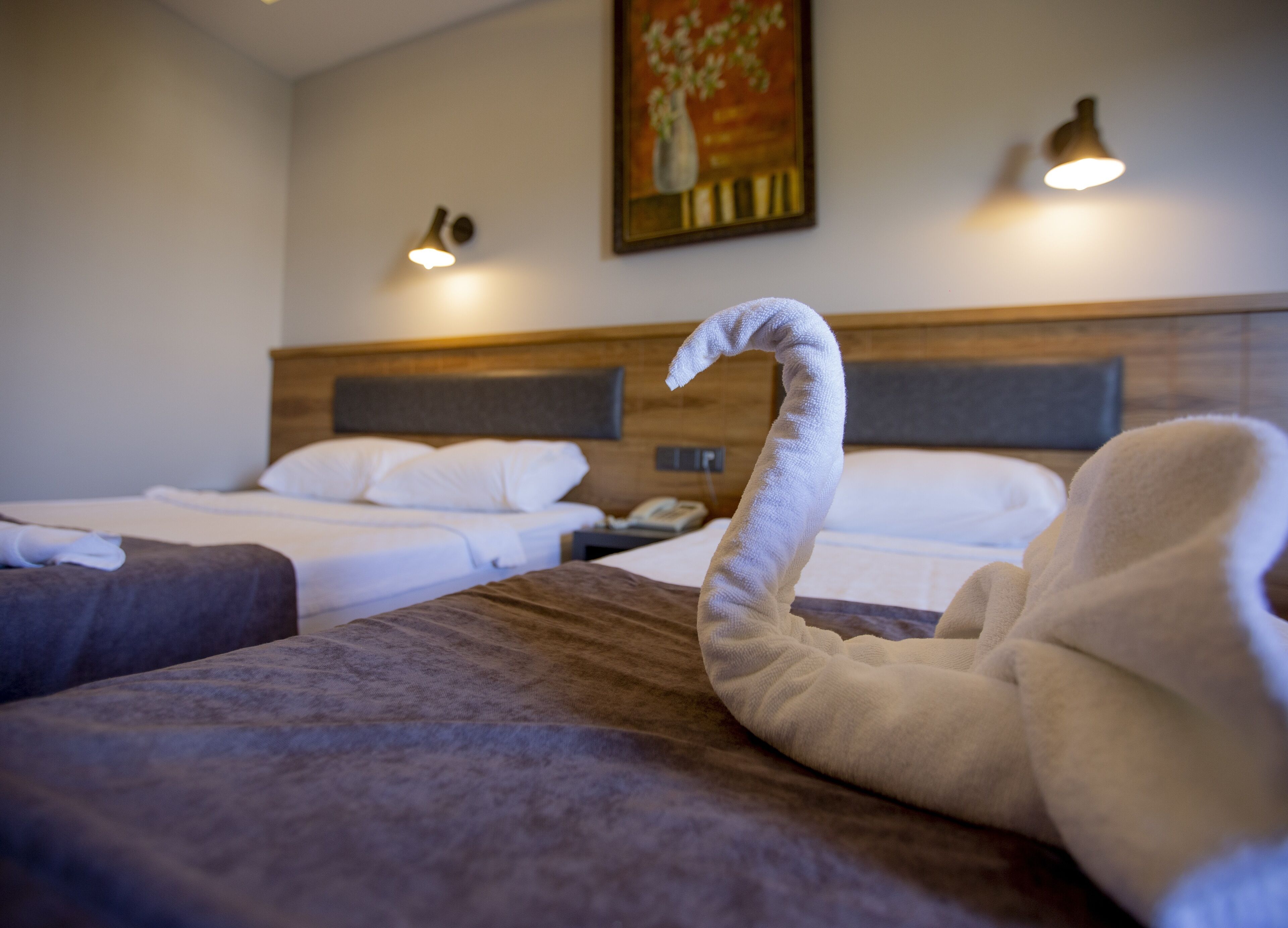 A hotel room with two beds, a painting on the wall, and two wall-mounted lamps.