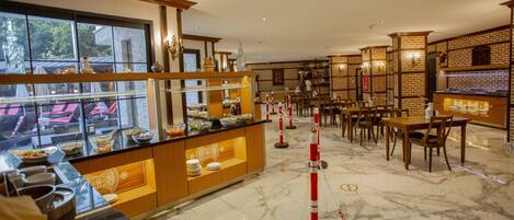 A restaurant with a marble floor, wooden furniture, and a buffet area with dishes displayed in glass cases.