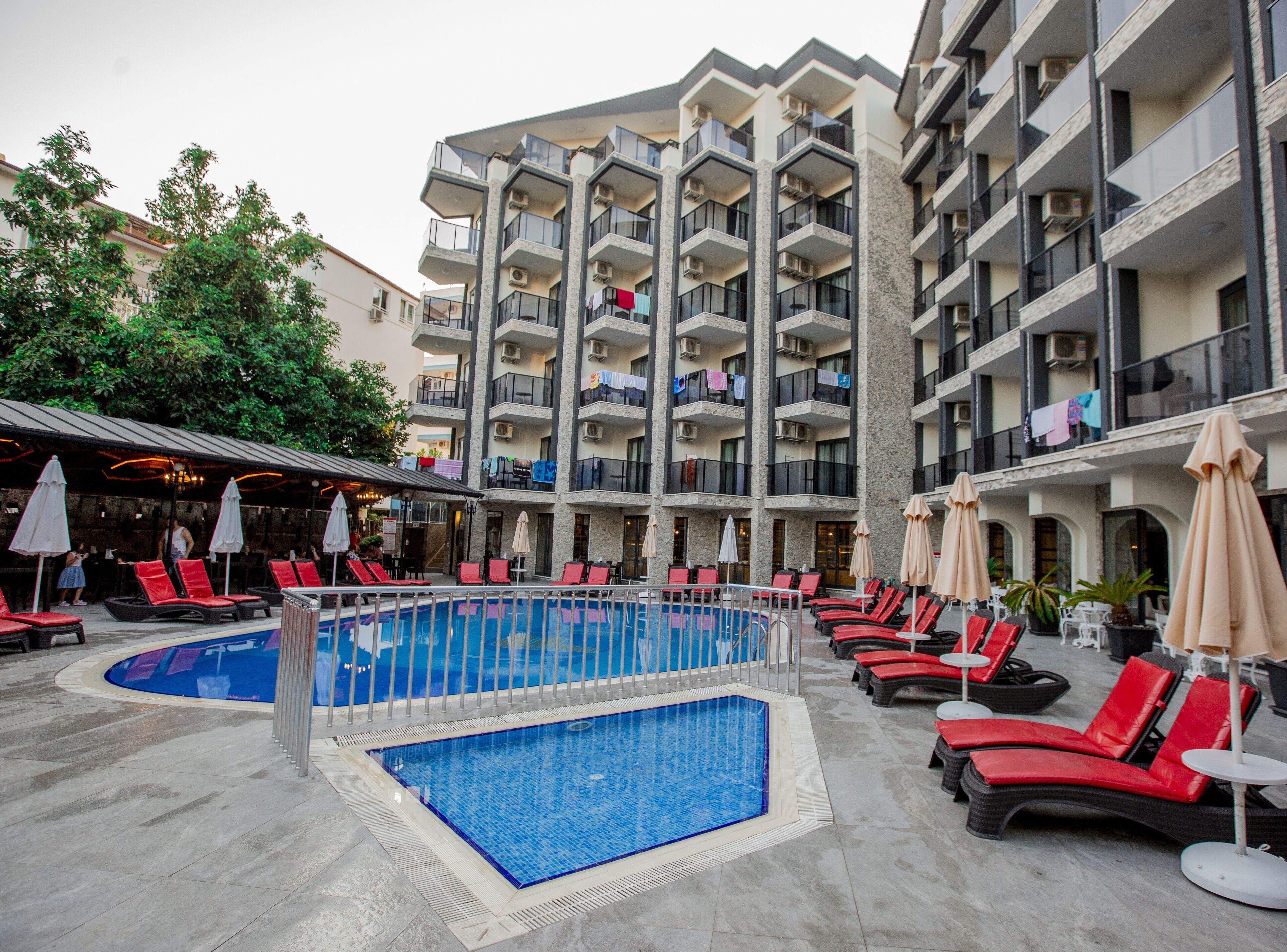 Ein Hotel mit Schwimmbad, roten Liegestühlen und mehreren Balkonen mit Klimaanlagen.