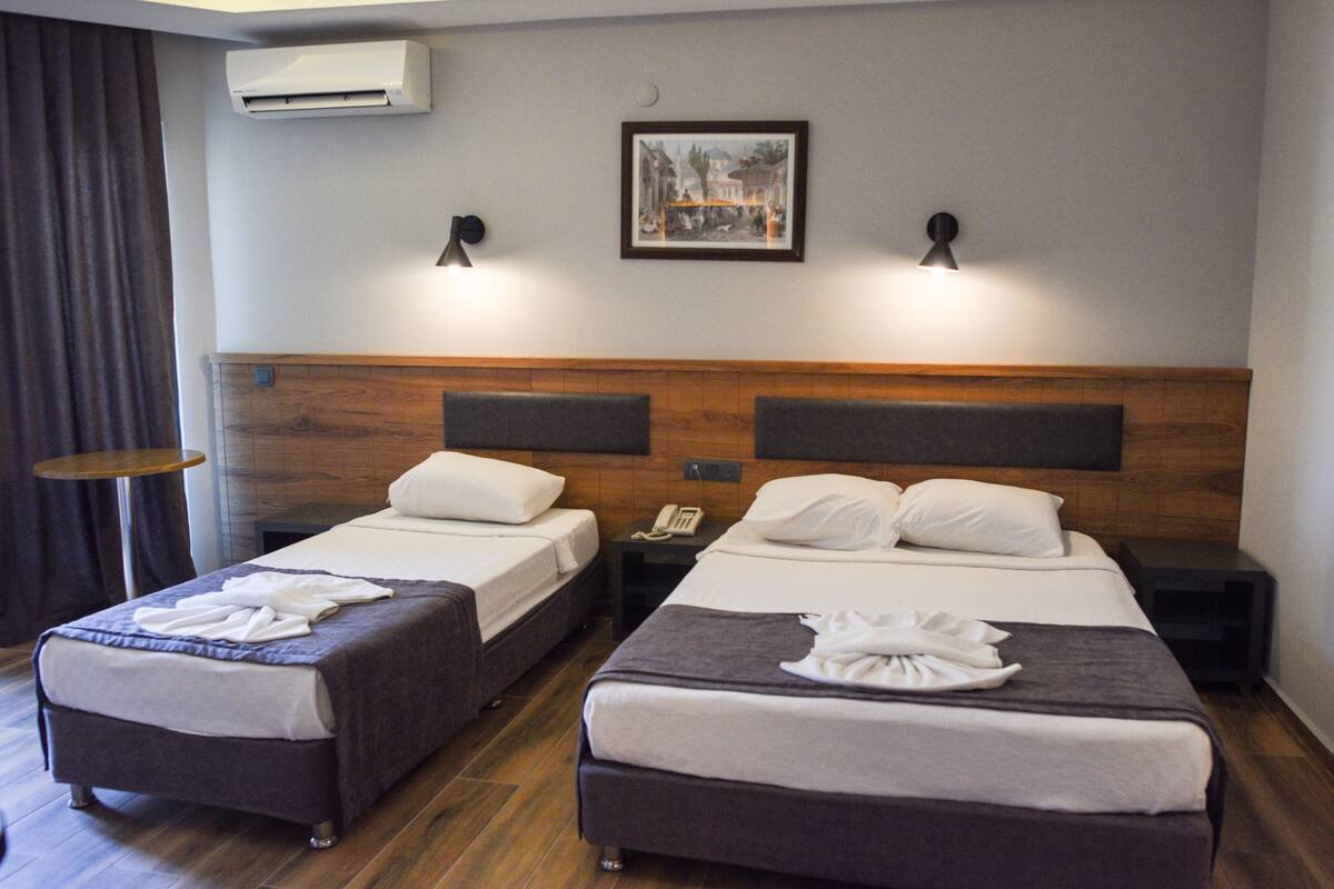 A hotel room with two beds, a wooden headboard, a framed picture on the wall, and a small table.