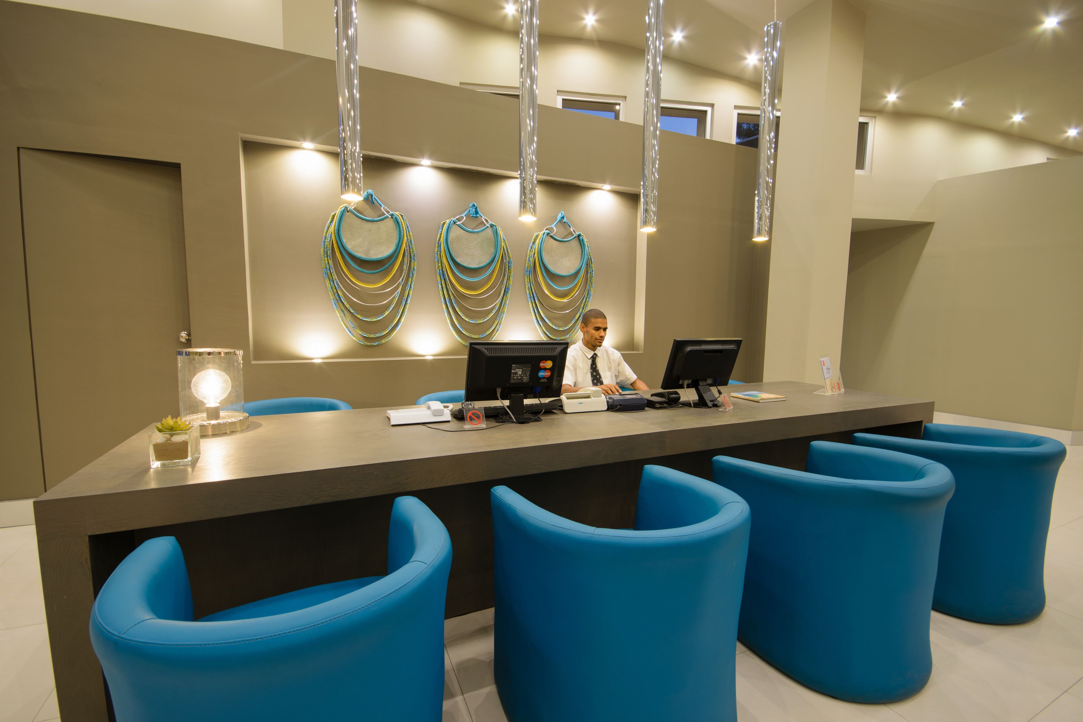 Un mostrador de recepción con una recepcionista, sillas azules y adornos en la pared.