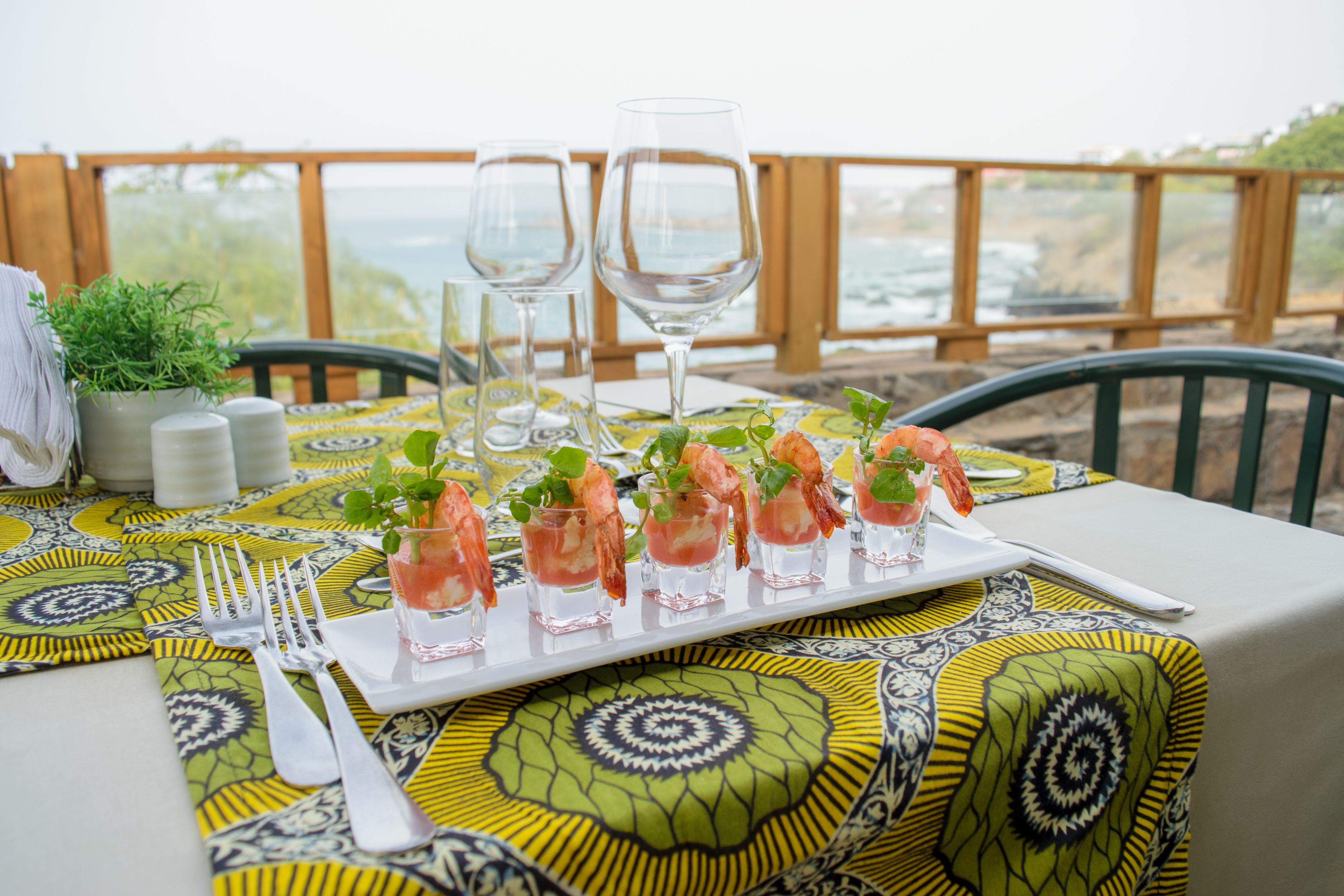 Una mesa dispuesta con un mantel estampado, un plato blanco con aperitivos de camarones, copas de vino y cubiertos.