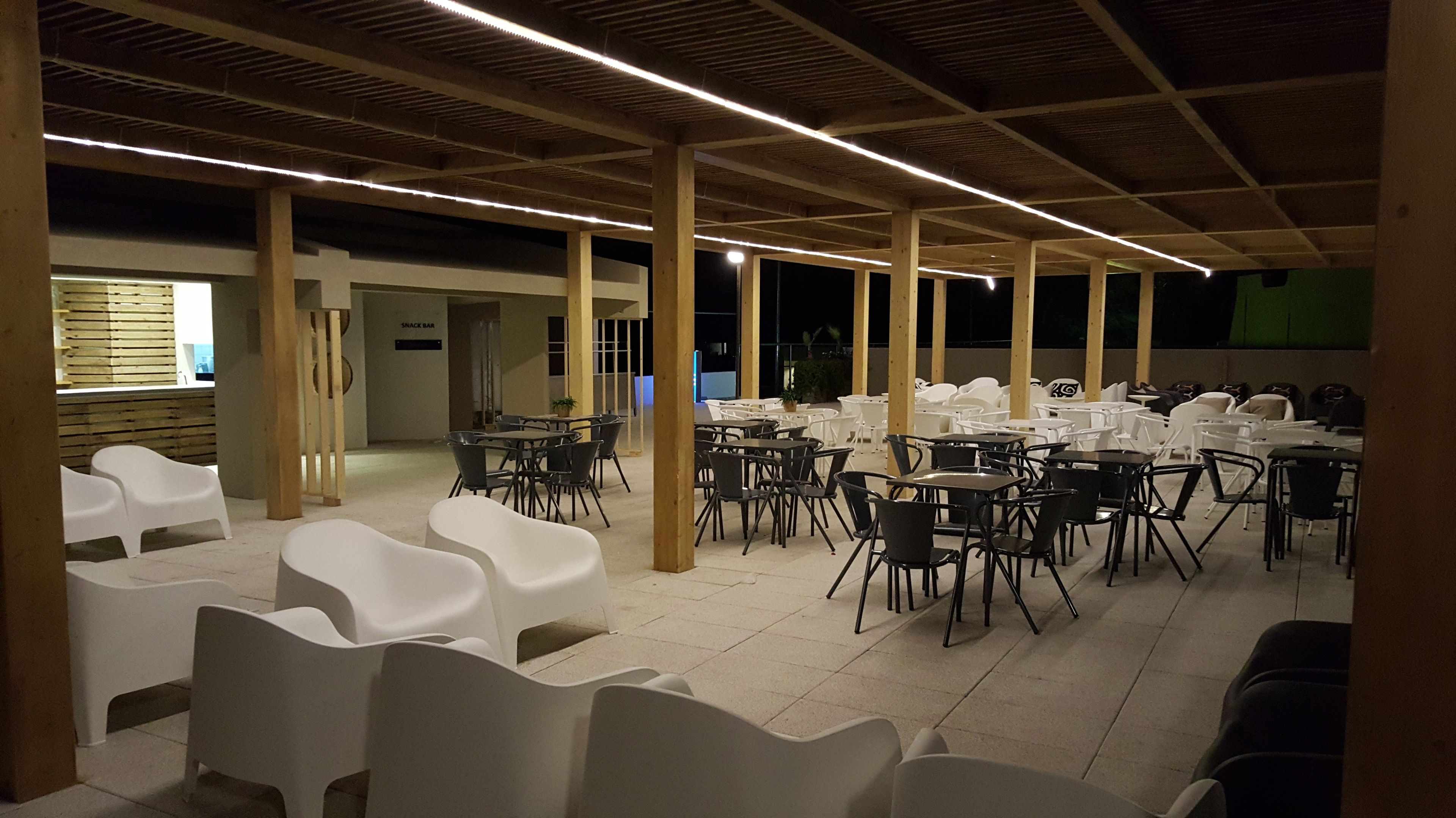 A spacious indoor dining area with multiple tables and chairs, wooden pillars, and a snack bar.