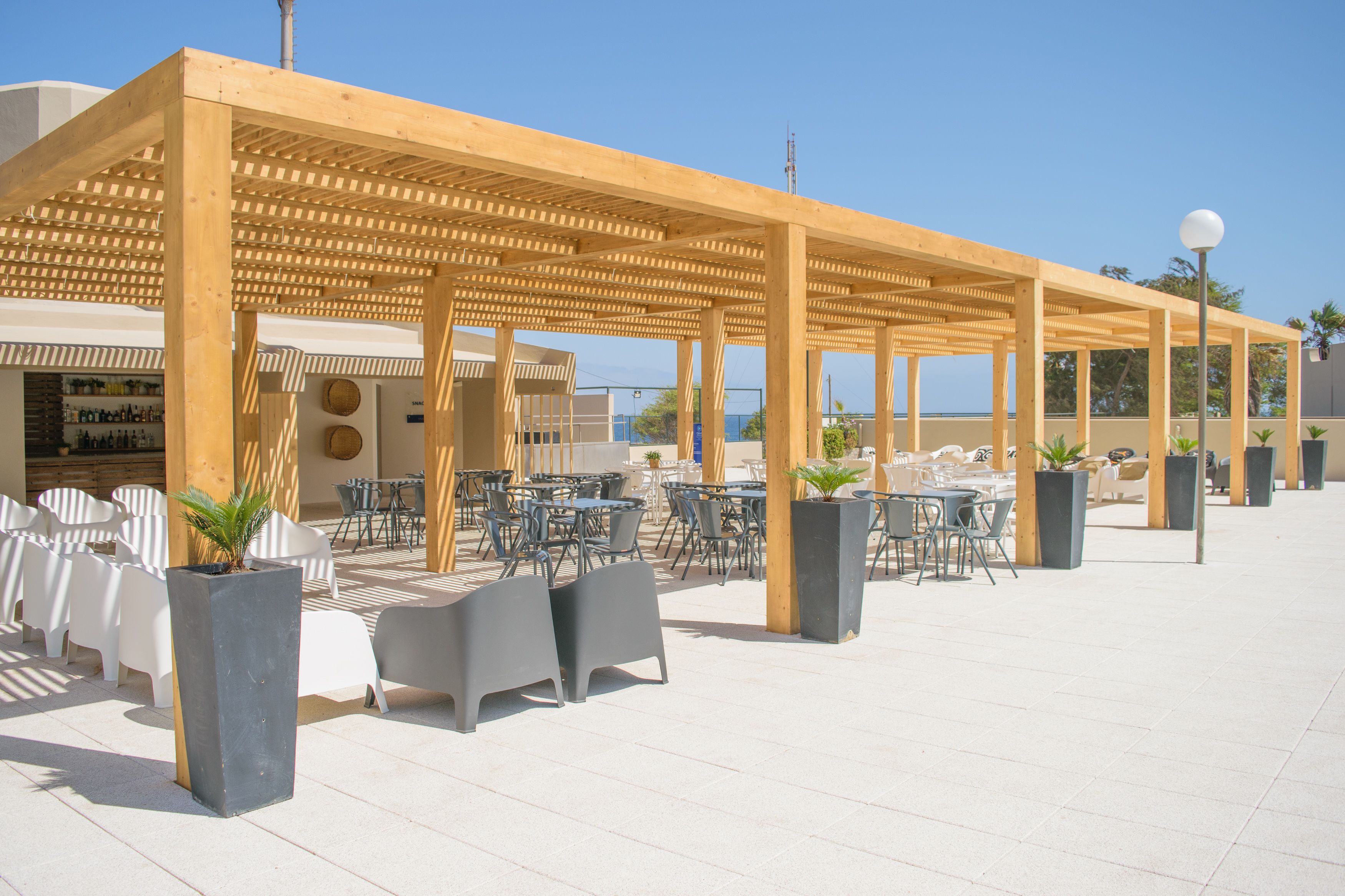 Un patio exterior con pérgolas de madera, sillas y mesas de plástico blanco.