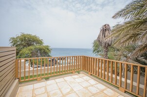 Un balcón con vista al mar, baranda de madera y suelo de baldosas.