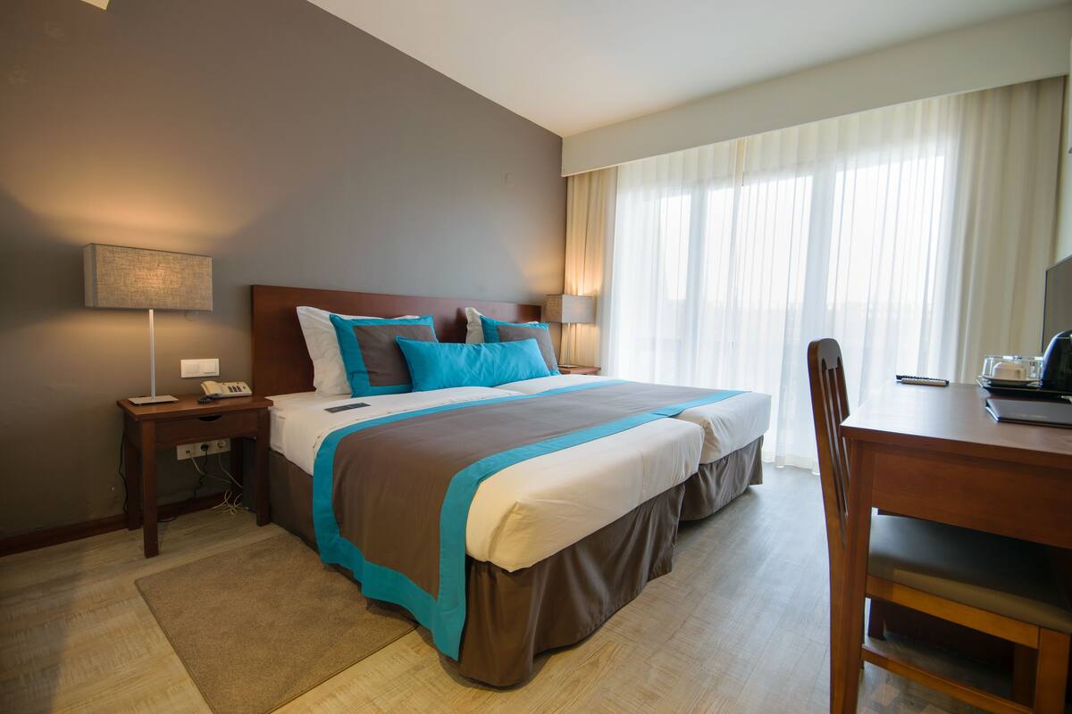 Habitación de hotel con una cama grande, un escritorio y una silla. Hay dos mesitas de noche con lámparas y un teléfono.
