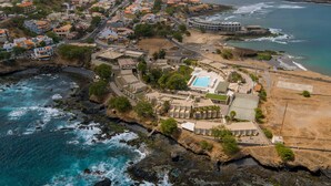 An aerial view of a coastal resort with a swimming pool, beachfront villas, and rocky terrain. - Hotel Oásis Atlântico Praiamar (Praia)
