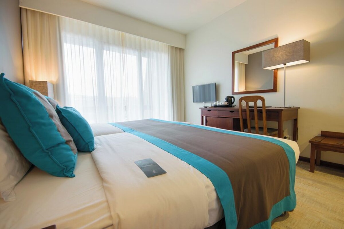 Una habitación de hotel con cama, escritorio, silla, televisor y lámpara.