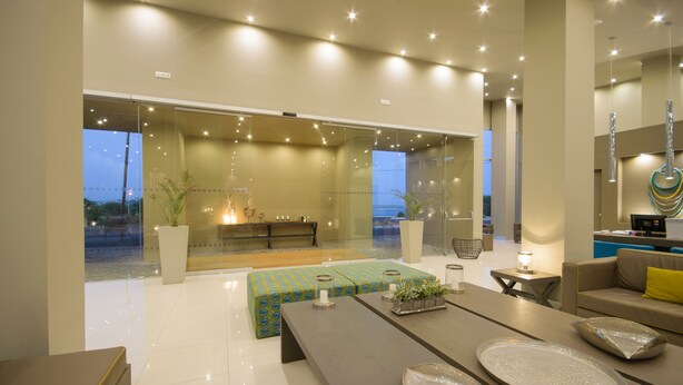 A modern living room with a glass wall, a sofa, a coffee table, and a dining area. - Hotel Oásis Atlântico Praiamar (Praia)