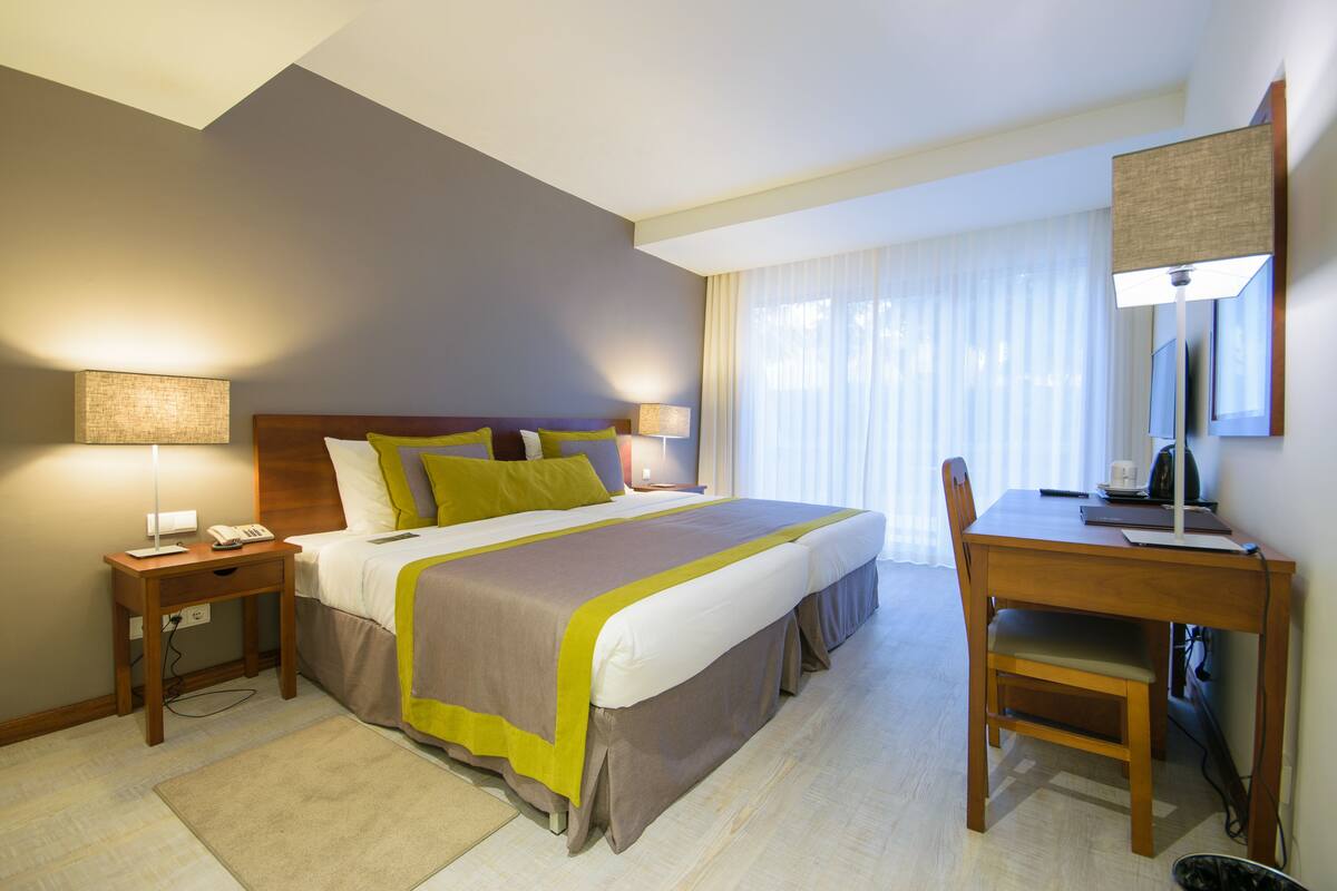 Una habitación de hotel con una cama grande, mesitas de noche con lámparas, un escritorio con una silla y un televisor.